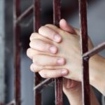 hands behind prison bars
