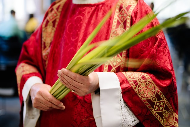 Priest wearing red vestments and carrying palm branches