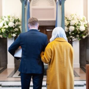 A couple approach a crematorium catafalque. The man is carrying a small white coffin.