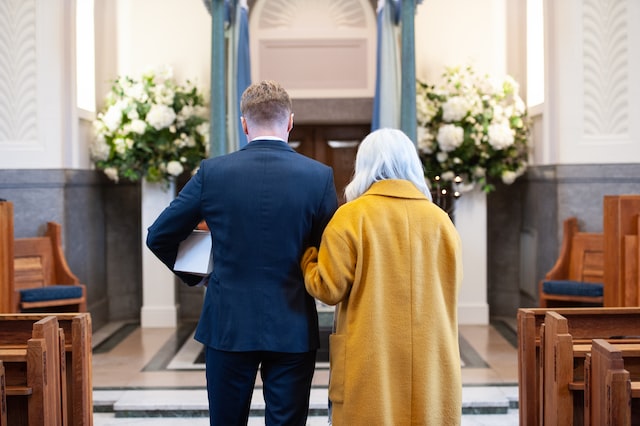 A couple approach a crematorium catafalque. The man is carrying a small white coffin.