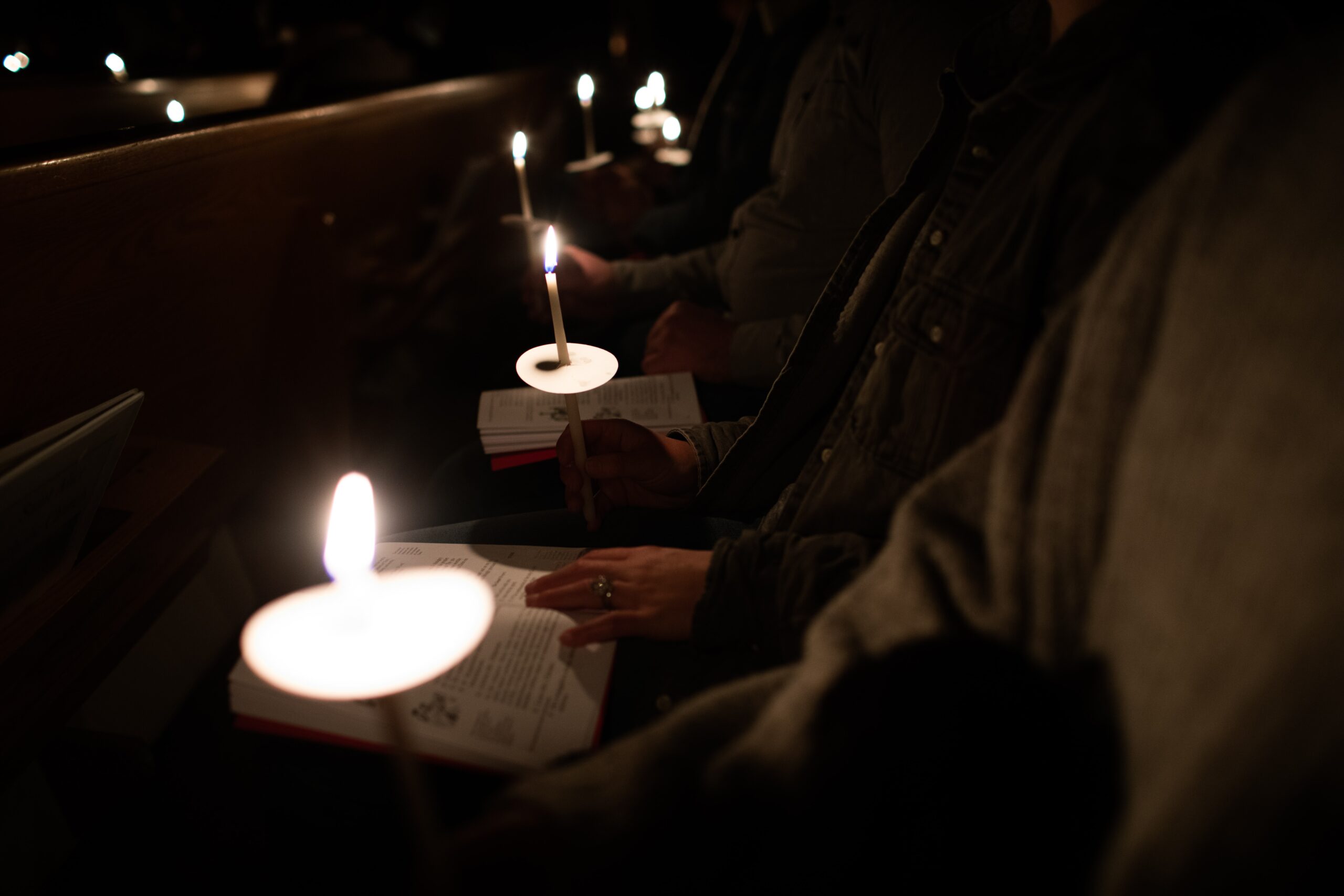 churchgoers in pews hold candles and songbooks