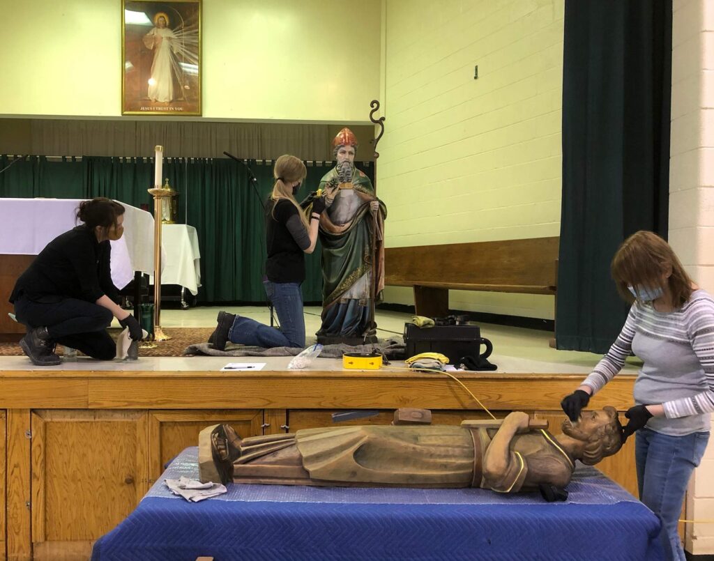 Three women clean statues in the parish hall of St. Patrick (Hubbard) after a church fire