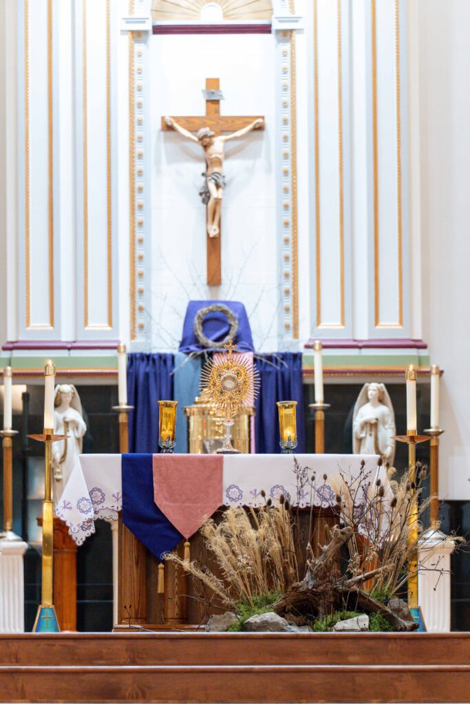 Eucharistic Adoration: monstrance on an altar with lit candles, purple cloths for Lent, and a crucifix behind