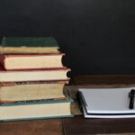 Piles of hard bound books beside an open notebook and pen