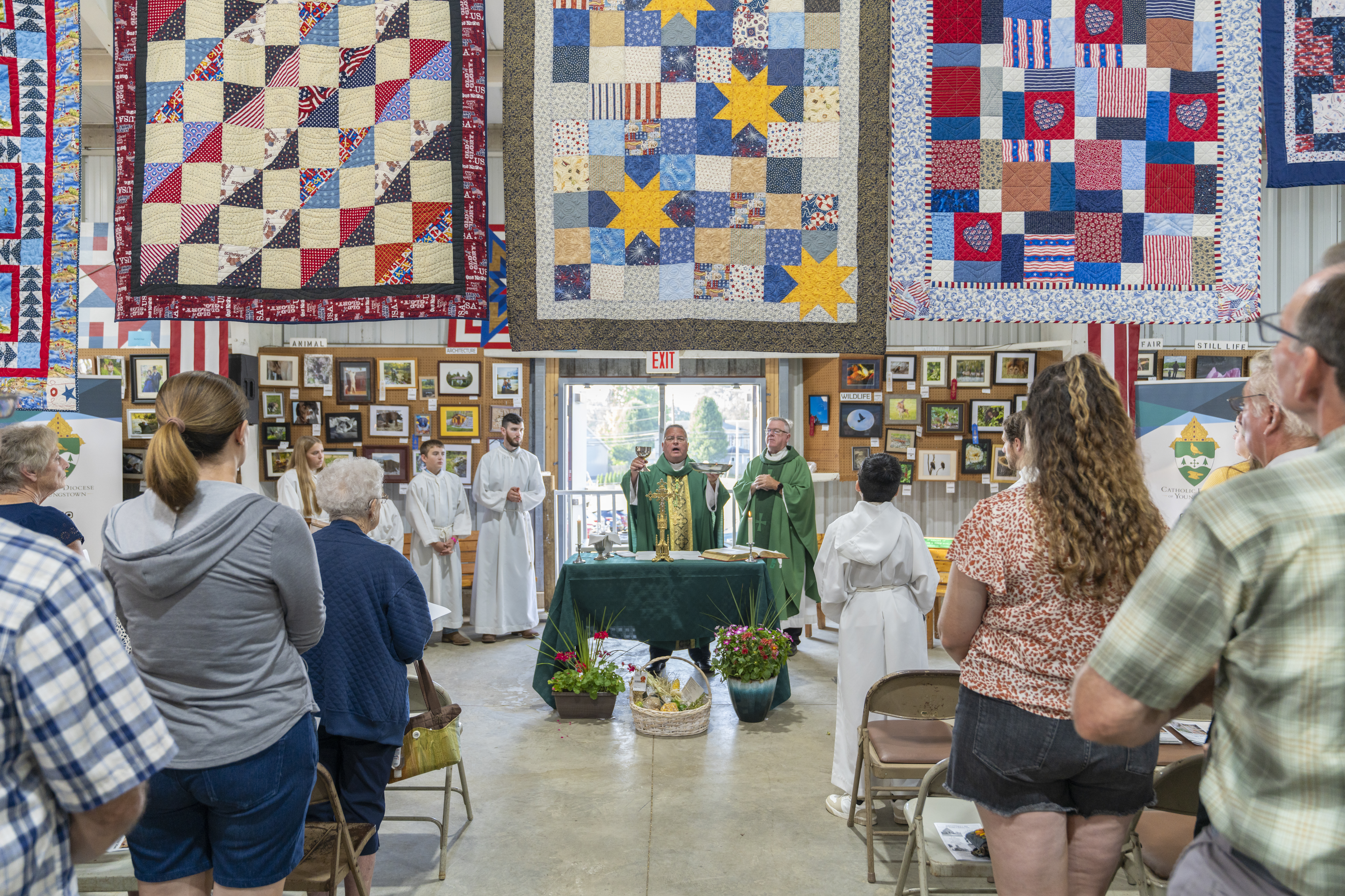 Bishop David Bonnar elevates the sacred vessels below a line of quialts and folding chairs full of participants in the Columbiana County Fair