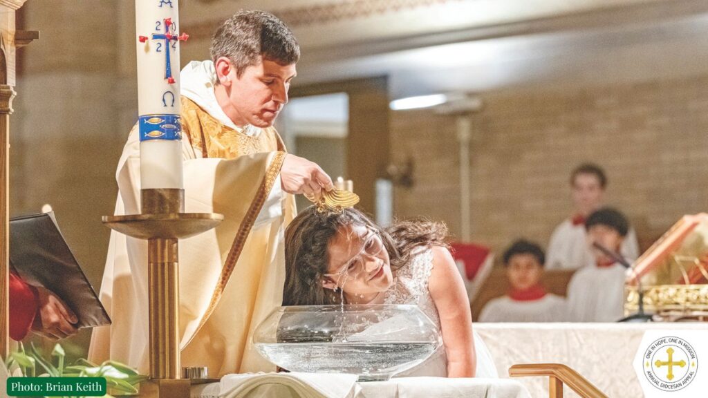 Father Frazzati in gold vestments pours water from a seashell over the head of a young woman wearing white to baptize her during Easter Vigil