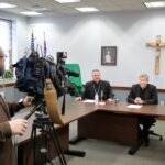 TV new camera films smiling Bishop and Vicar General with crucifix in the background