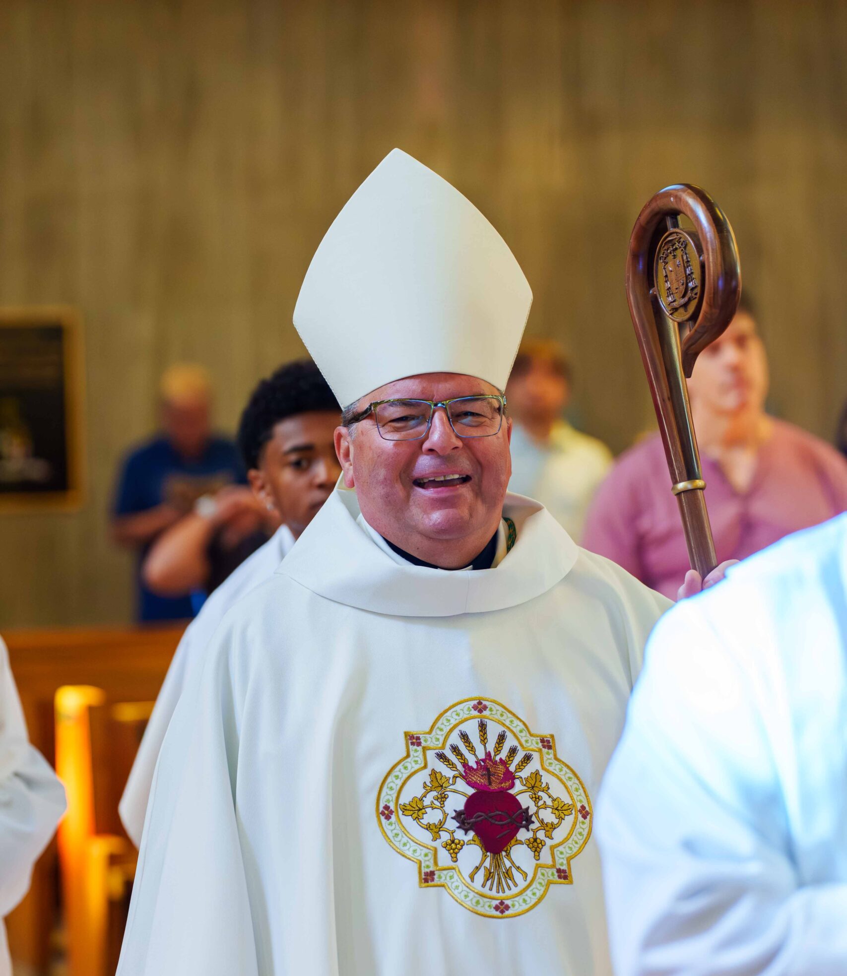 Bishop David J Bonnar smiling in white vestments embroidered with the Sacred Heart