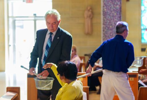 Ushers pass the baskets for the collection as parishioner donates her tithe