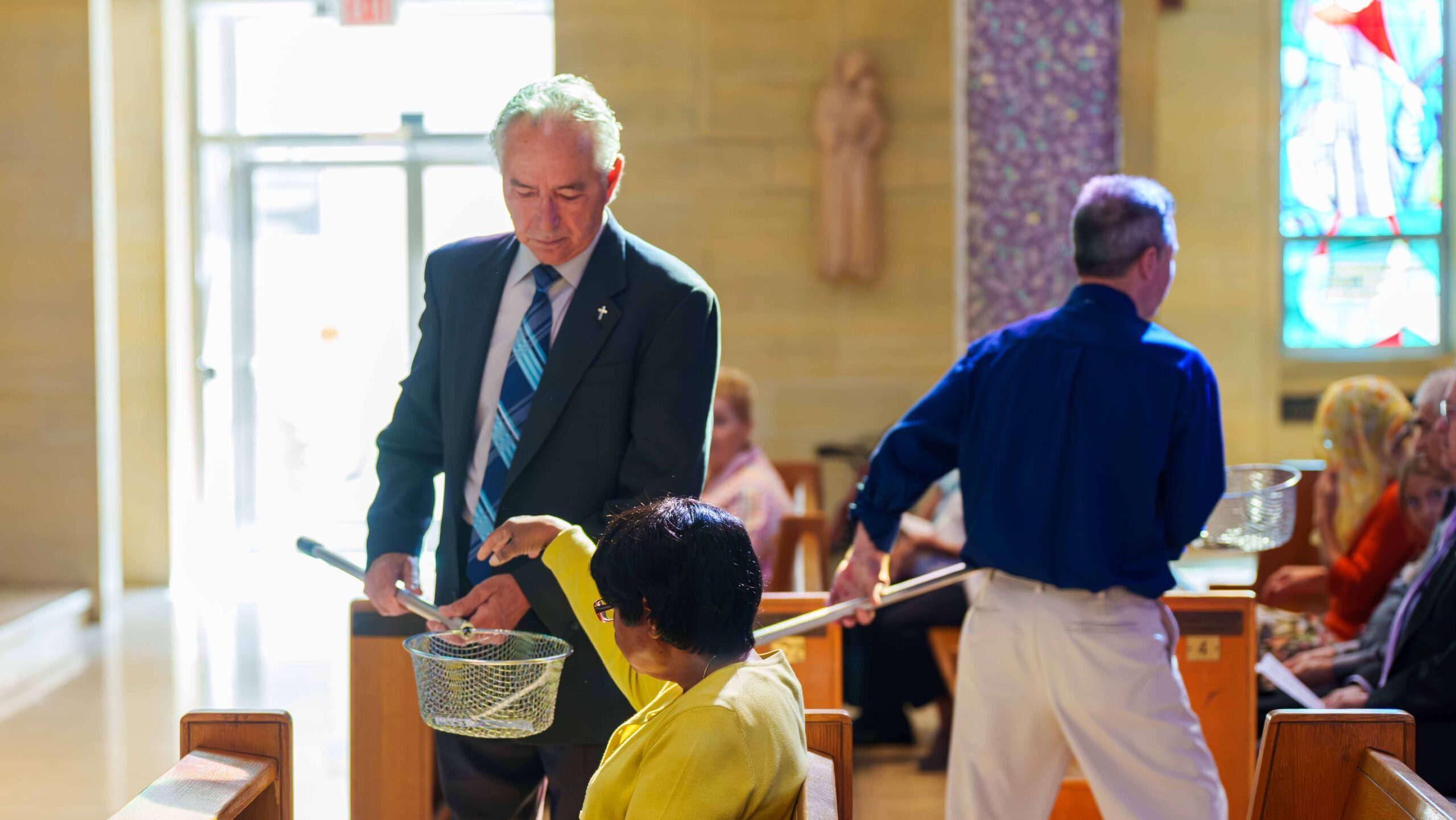 Ushers pass the baskets for the collection as parishioner donates her tithe