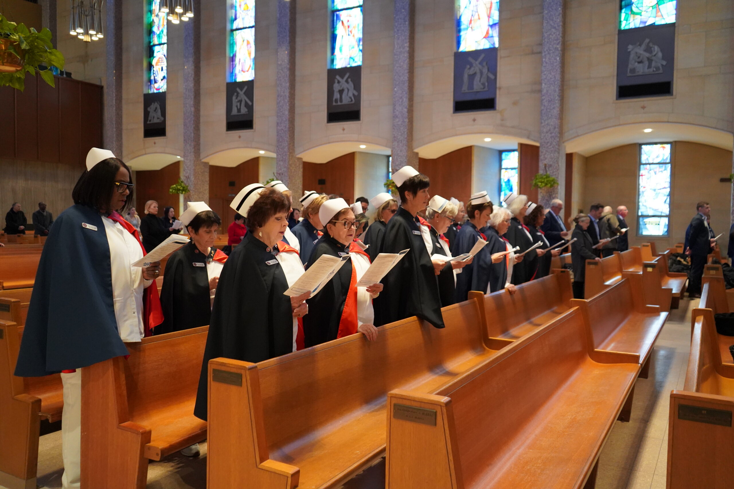 Women wearing black caps and white hats stand in pews at Saint Columba Cathedral, singing along with an order of service